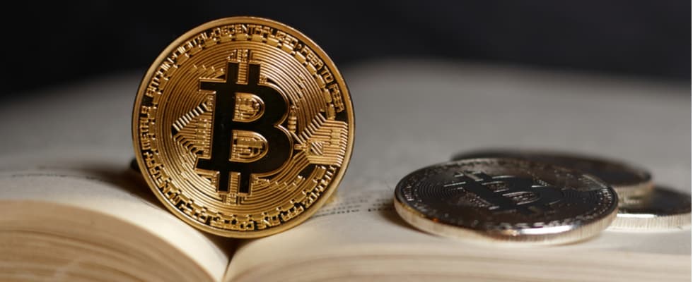 A gold Bitcoin coin on an open book highlights the appeal to buy bitcoin from Coinmama.